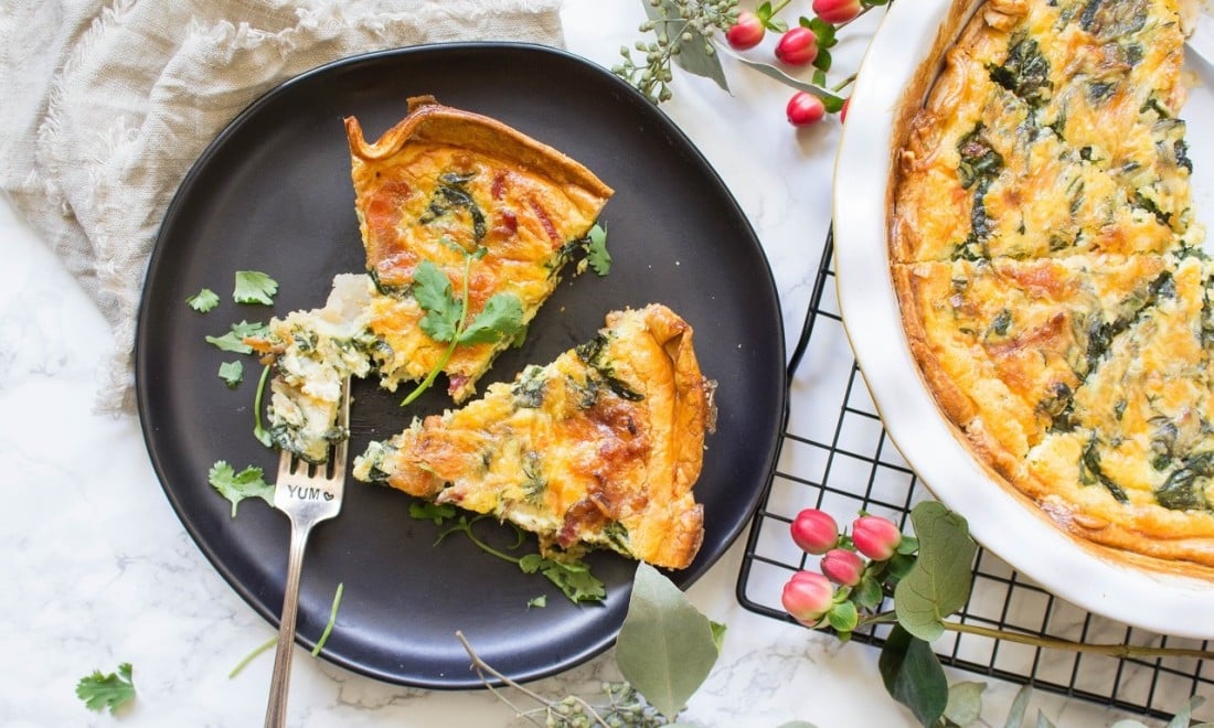 Two Pieces Of Spinach And Bacon Quiche Served On Black Plate